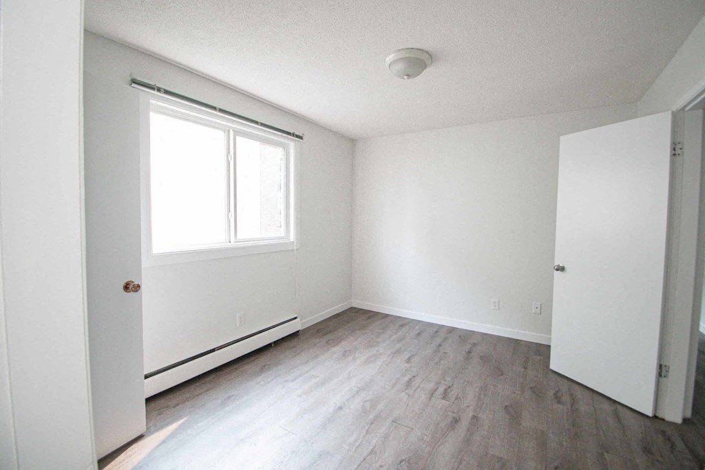 an empty room with white walls and a window and wood floors