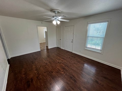 an empty living room with wood floors and a ceiling fan