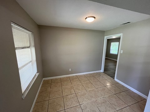 A room with beige tiles on the floor and a window with blinds.