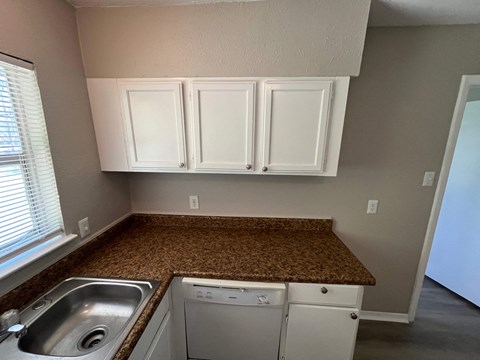 A kitchen with white cabinets and a brown countertop.