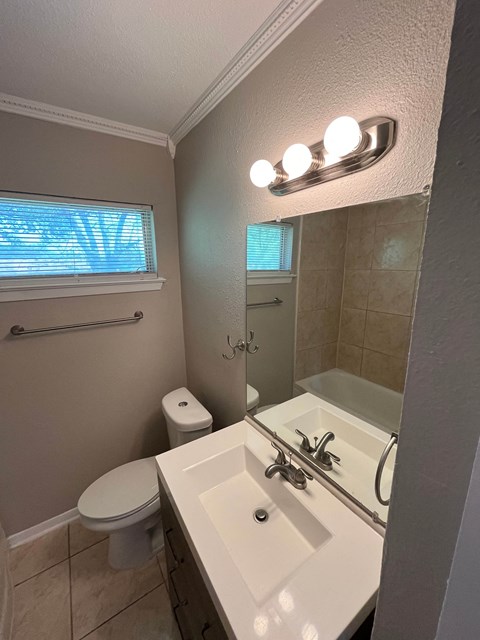 A bathroom with a toilet, sink, mirror, and window.