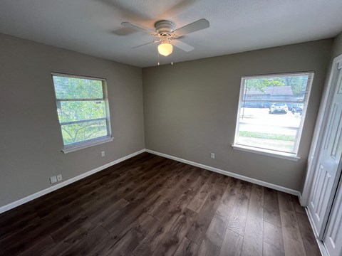 A room with a ceiling fan and two windows.