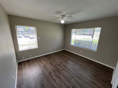 A room with a ceiling fan and two windows.