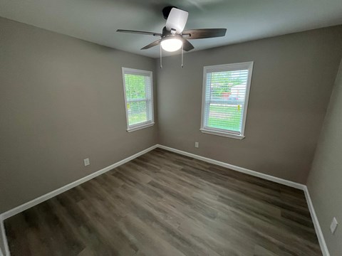 A room with a ceiling fan and two windows.