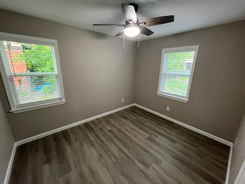 A room with a ceiling fan and two windows.
