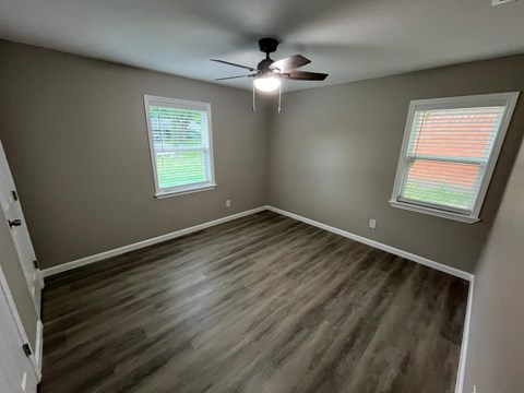 A room with a ceiling fan and two windows.