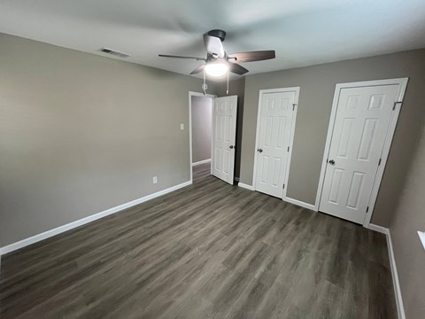 A room with a ceiling fan and three doors.