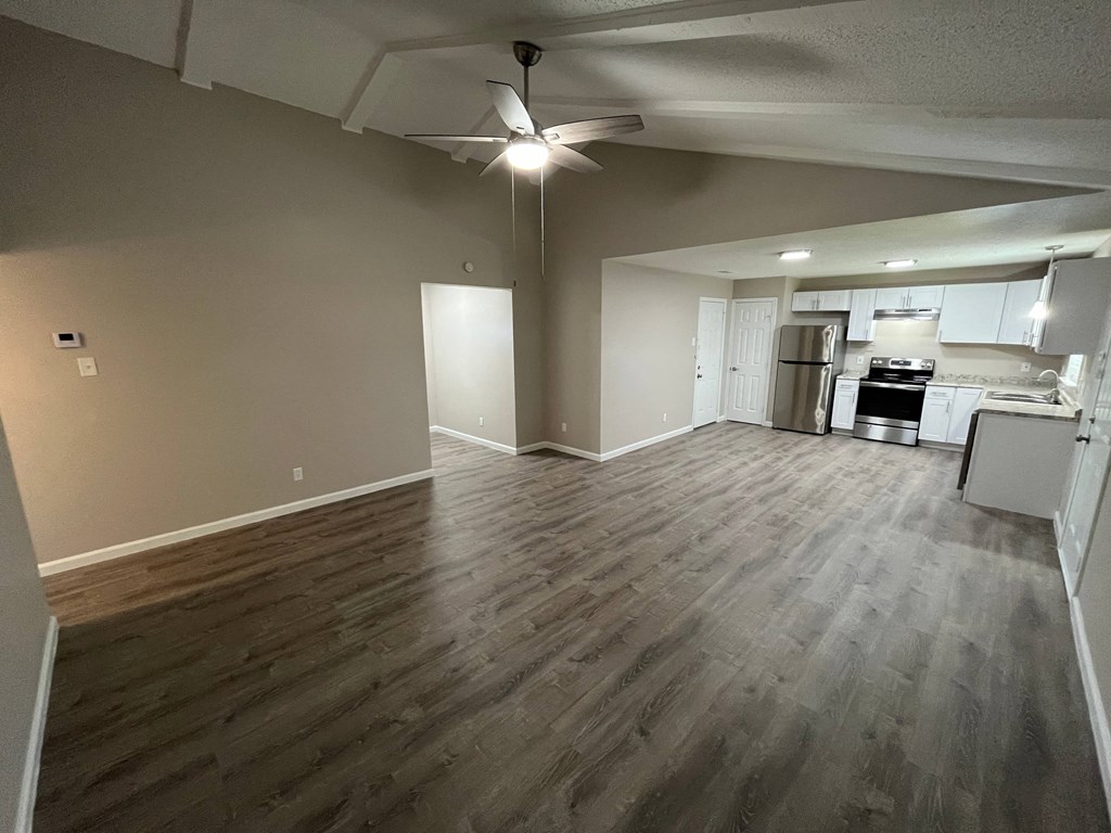 A room with a kitchen in the background and a wood floor.