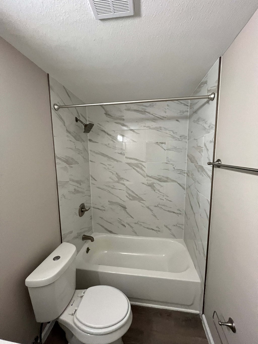 A white toilet sits next to a bathtub in a small bathroom.