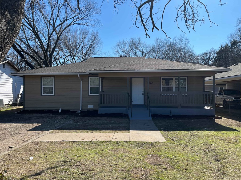 A house with a gray roof and a white door is surrounded by a grassy area.