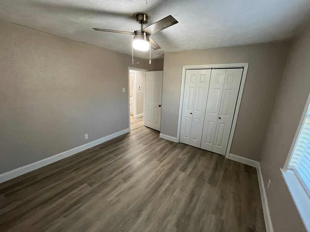 A room with a ceiling fan and light fixture, wooden flooring, and two white doors.