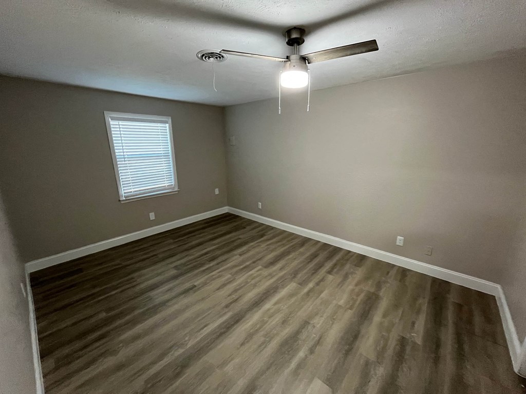 A room with a ceiling fan and wooden flooring.