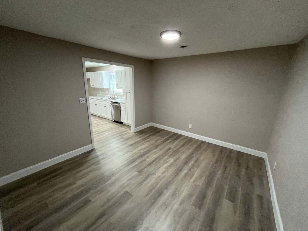A room with wooden flooring and a view into another room through an open door.