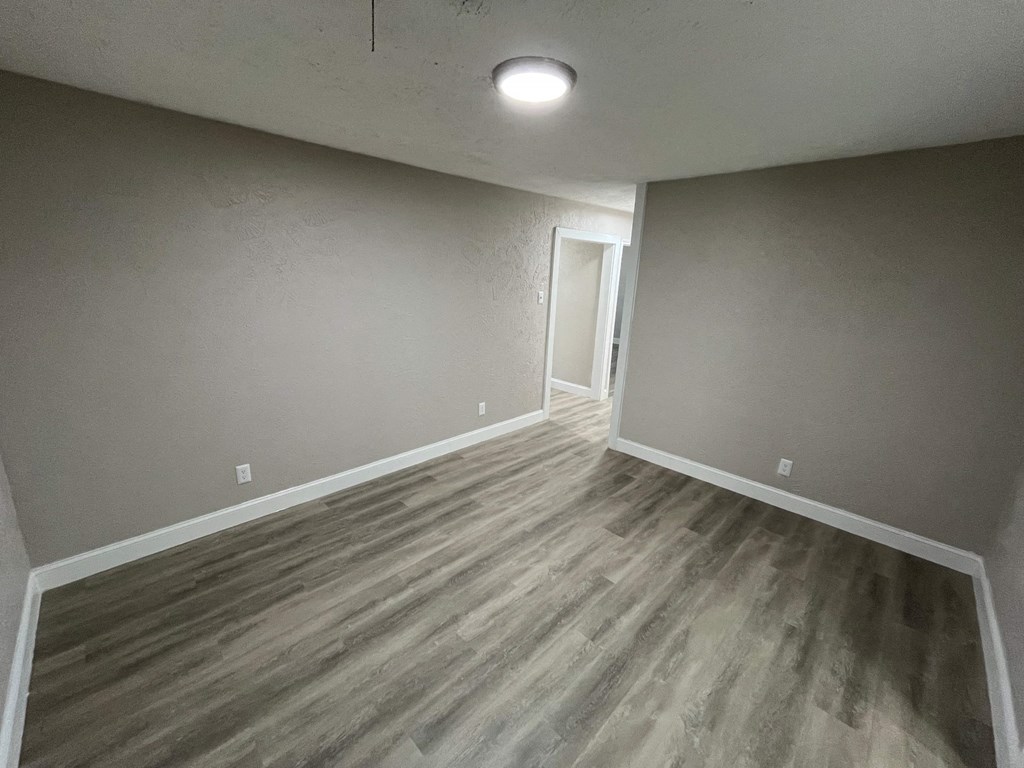 A room with a wooden floor and a doorway leading to another room.