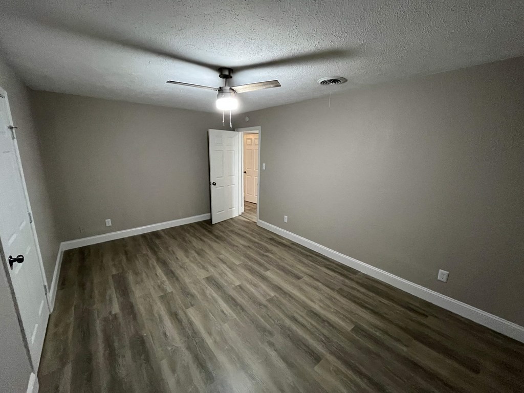 A room with a ceiling fan and light fixture, and a door at the end of the room.