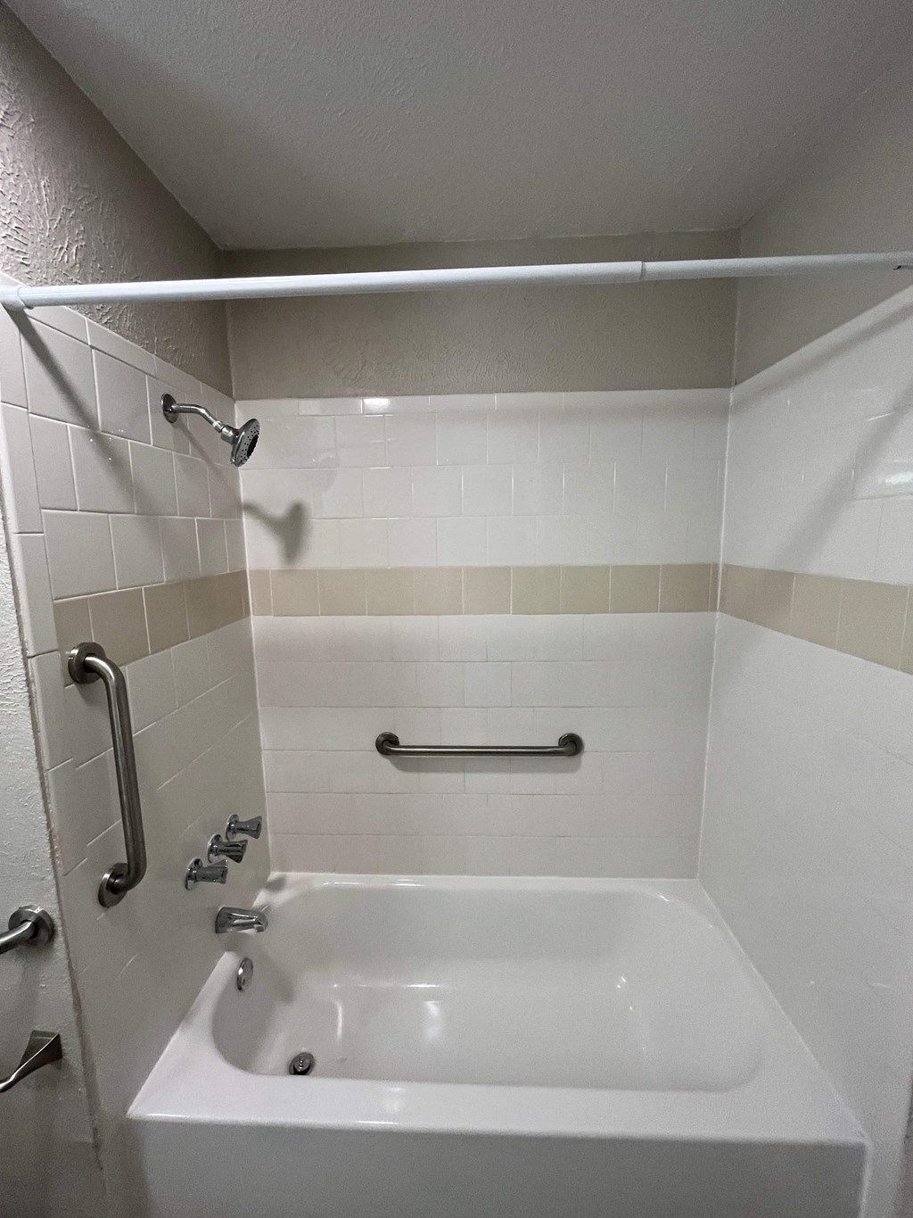 A white bathroom with a white tub and silver grab bars.