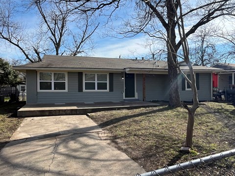 A grey house with a red door and a tree in front.