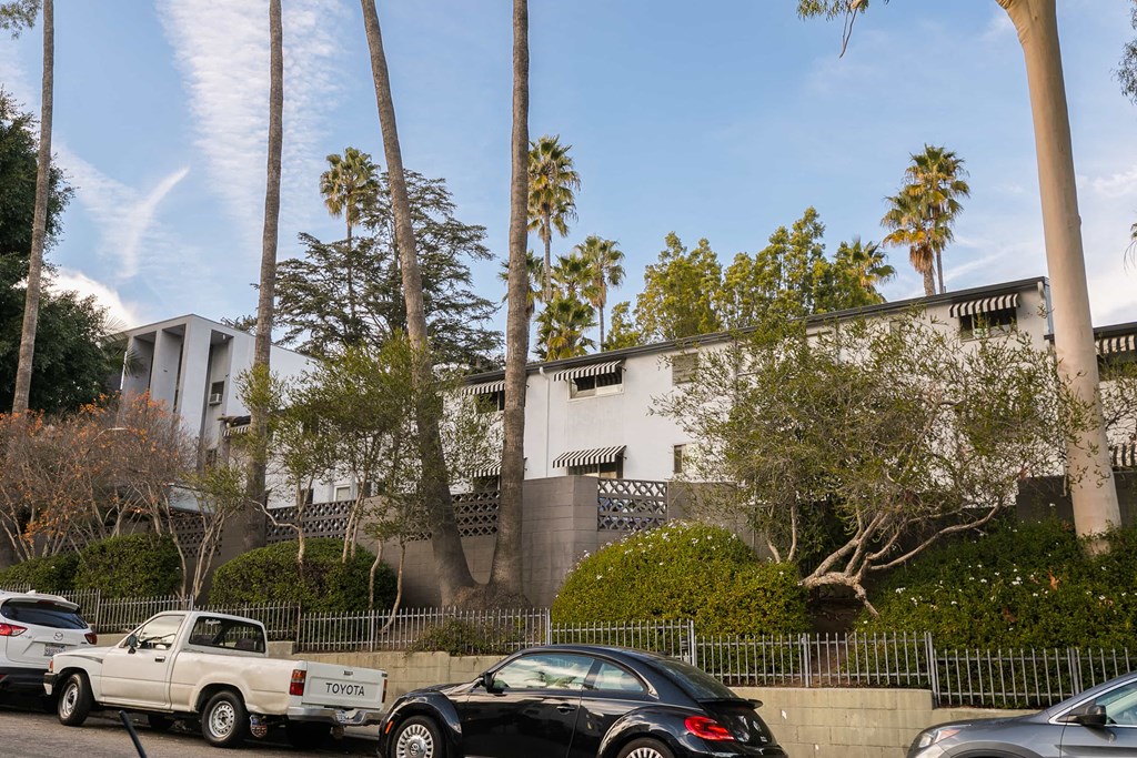 an apartment building with palm trees and cars parked in front
