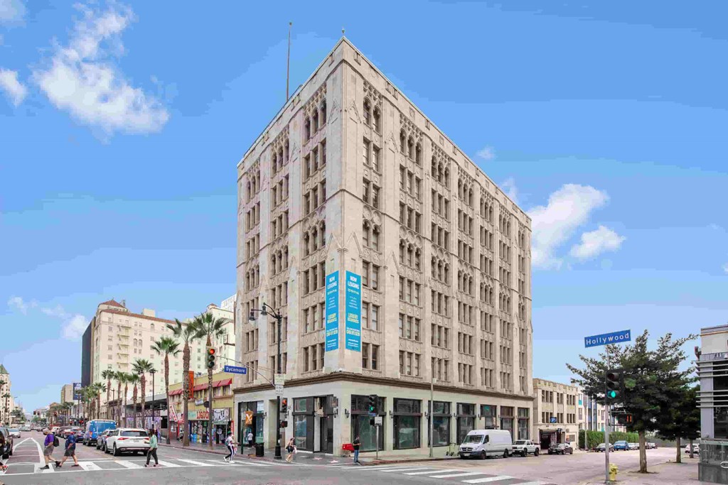 a large white building with a blue sign on the corner of a city street