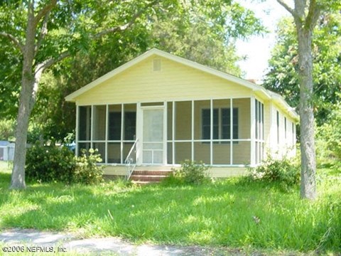 A yellow house with a porch and a tree in front.