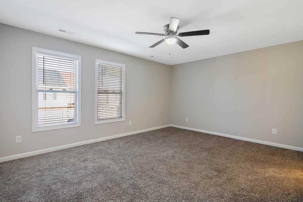 an empty living room with a ceiling fan and two windows