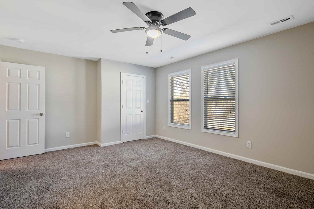 an empty living room with a ceiling fan and three windows