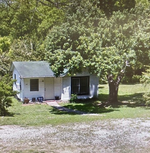A small white house with a porch and a tree in front.
