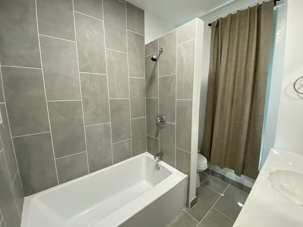 A white bathtub sits in a bathroom with grey tiles.