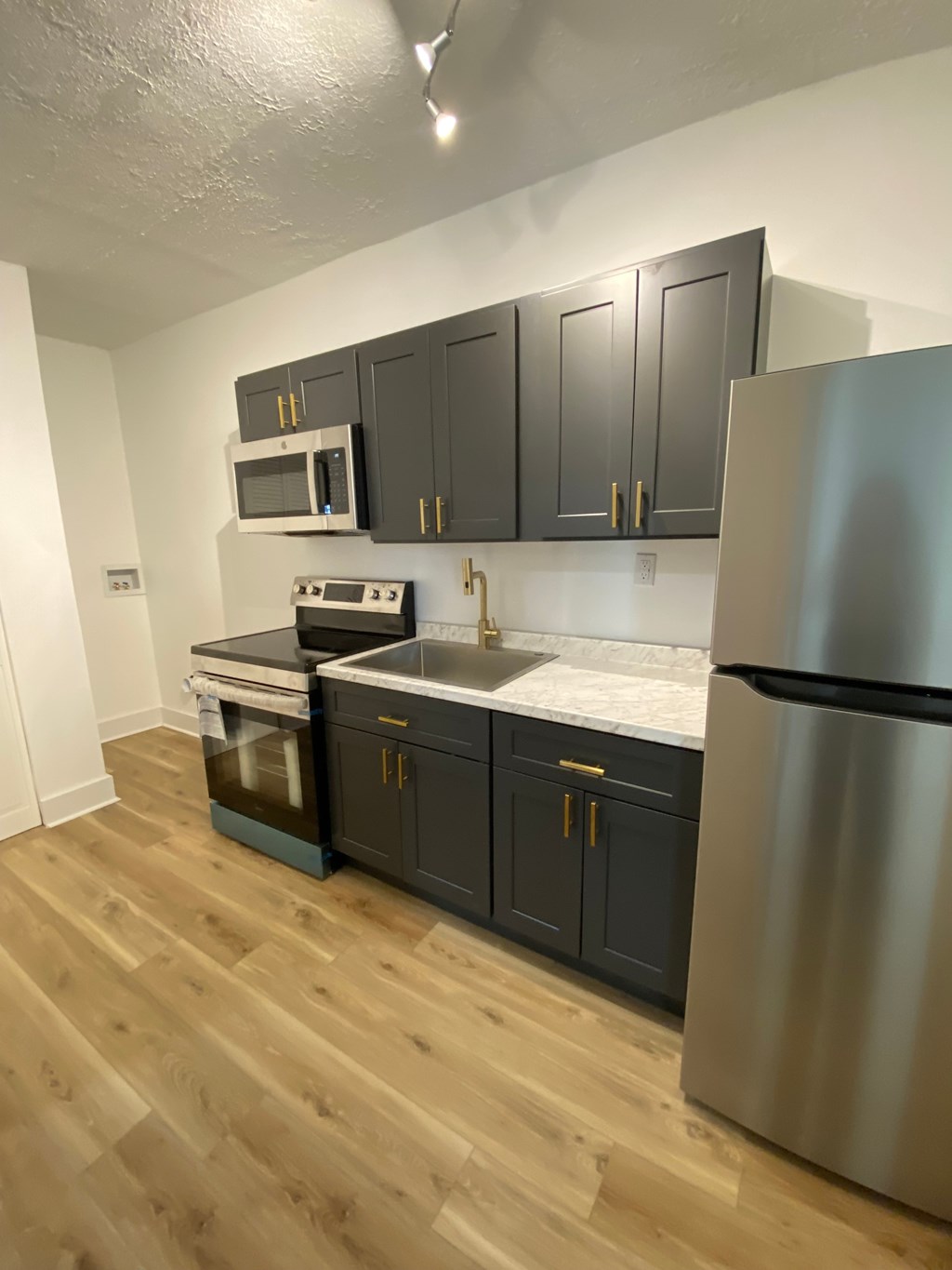 A kitchen with a stainless steel refrigerator, black cabinets, and wooden flooring.
