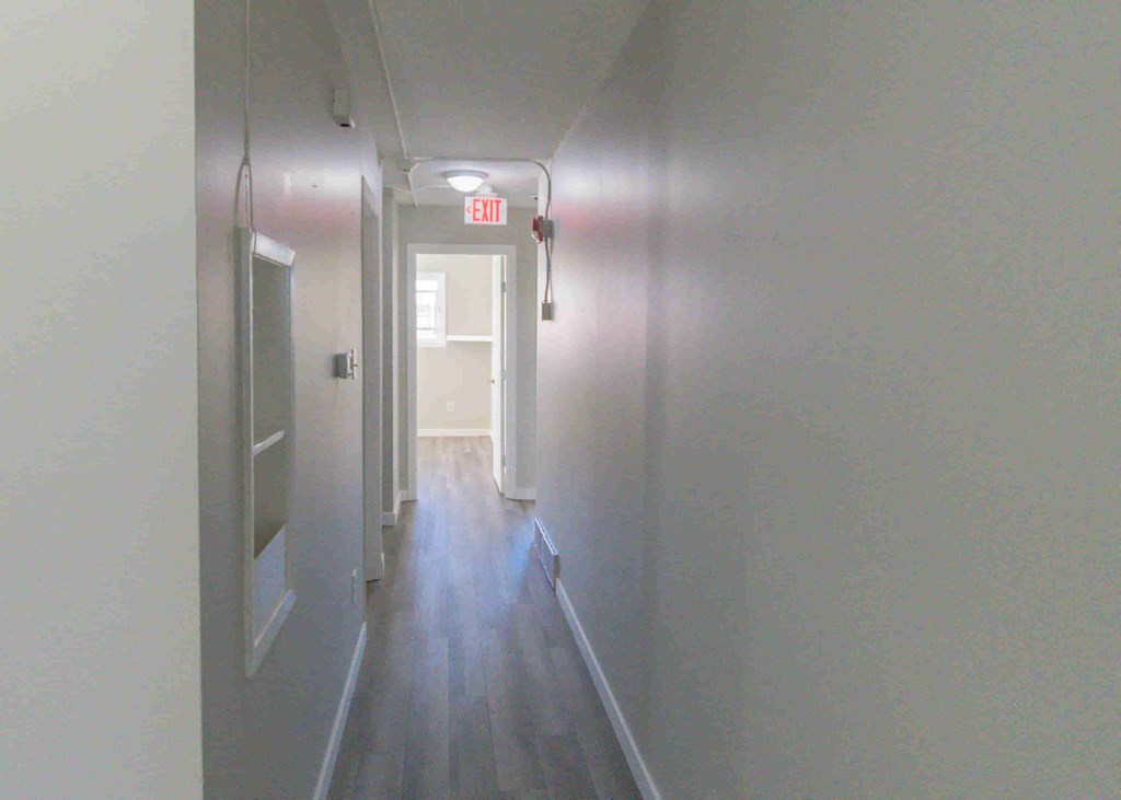 a long hallway with white walls and wood floors and an exit sign