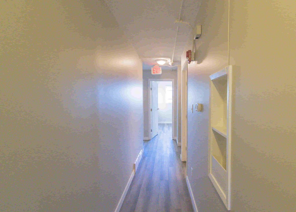 a hallway with white walls and a wooden floor and a door