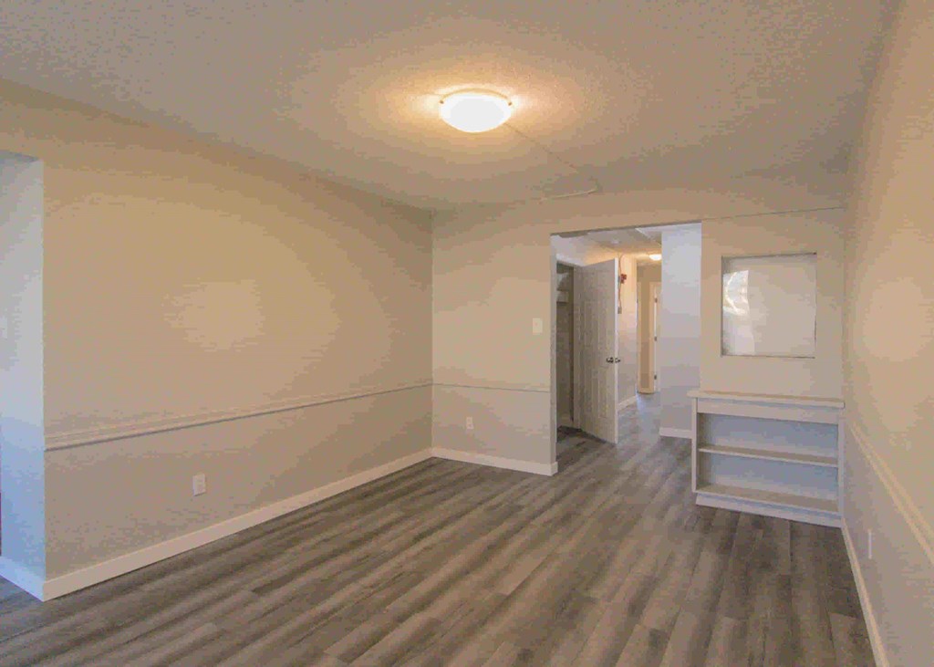 a room with white walls and wooden floors and a door to a closet