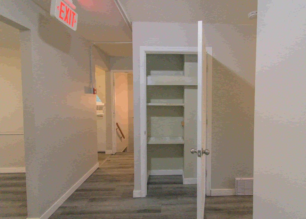 an open closet in a hallway with stairs and a exit sign