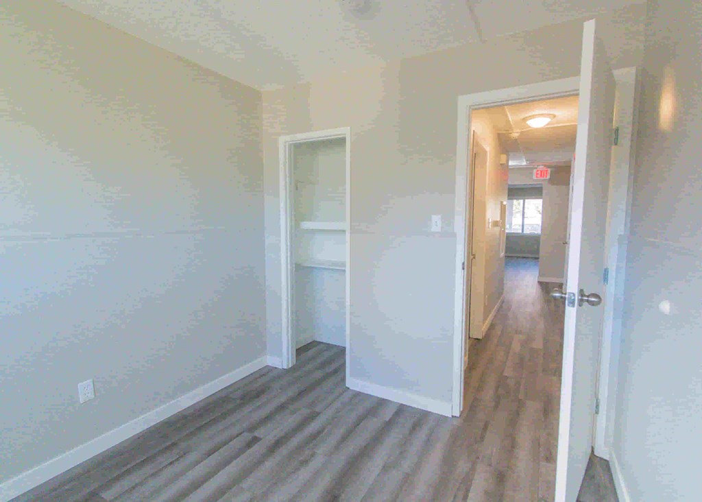 a hallway with white walls and wood floors      and a closet