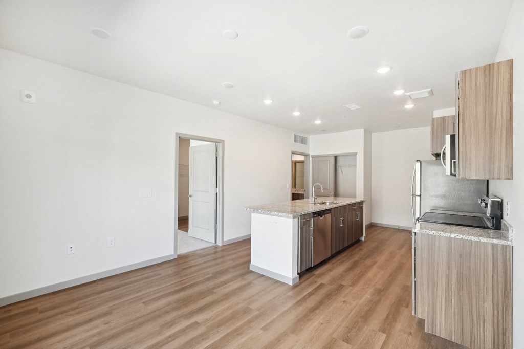 a renovated living room with a kitchen with wood flooring and white walls