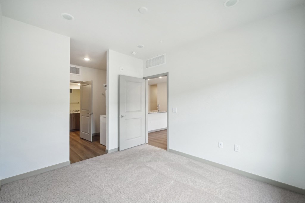 an empty living room with white walls and a door to a bathroom