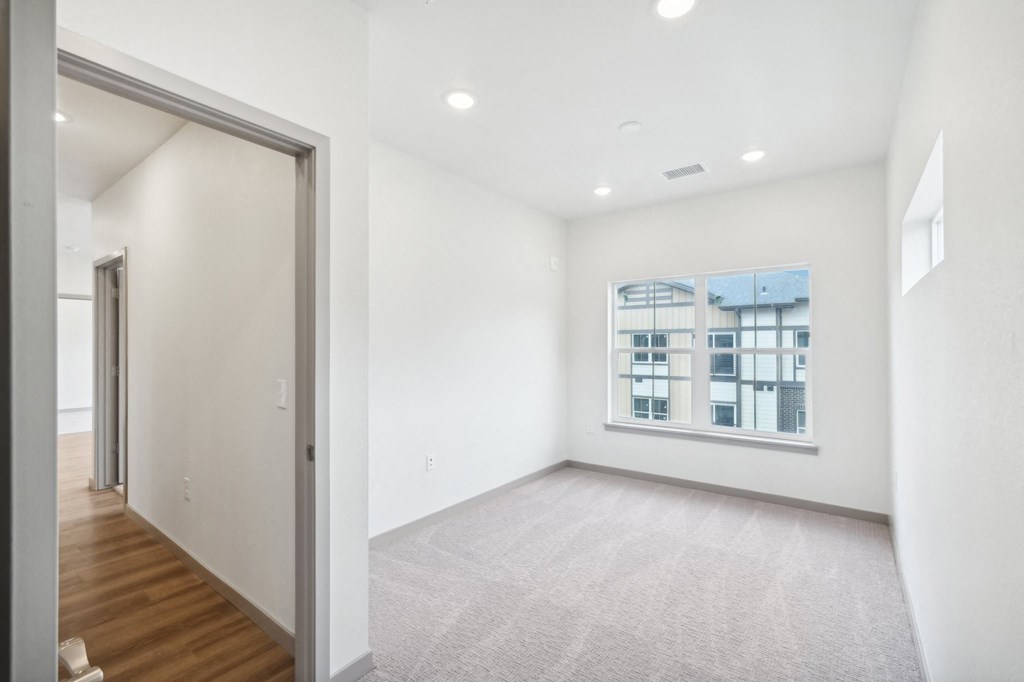 an empty living room with a window and a door to a bedroom