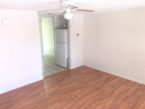 an empty living room with a hard wood floor and a refrigerator