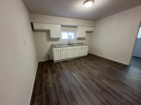 an empty kitchen with white cabinets and a wooden floor