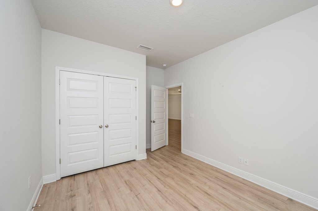a bedroom with white walls and wood flooring and a closet