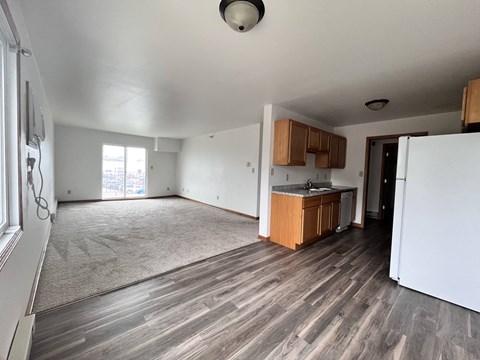 an empty living room and kitchen with wood flooring and white walls