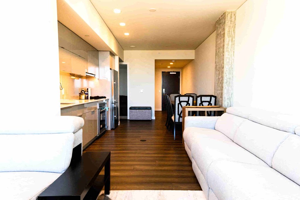 A white couch sits in a modern living room with a kitchen area in the background.