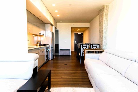 A white couch sits in a modern living room with a kitchen area in the background.