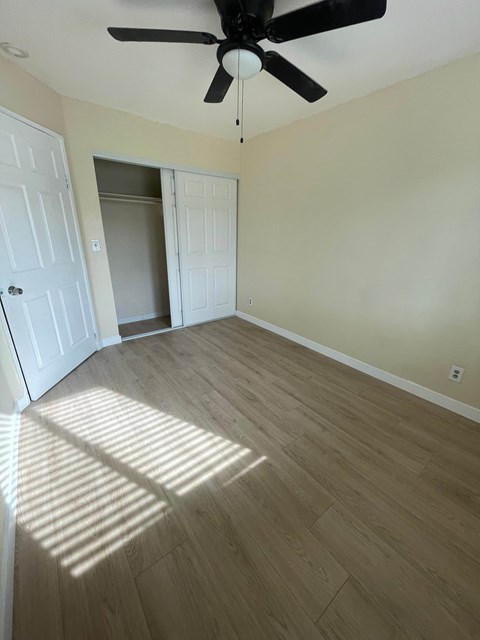 A room with a ceiling fan and light, and a wooden floor.