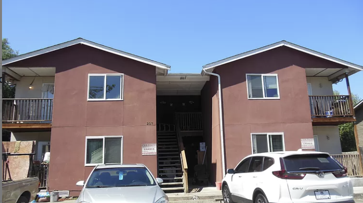 Two cars are parked in front of a two-story building.