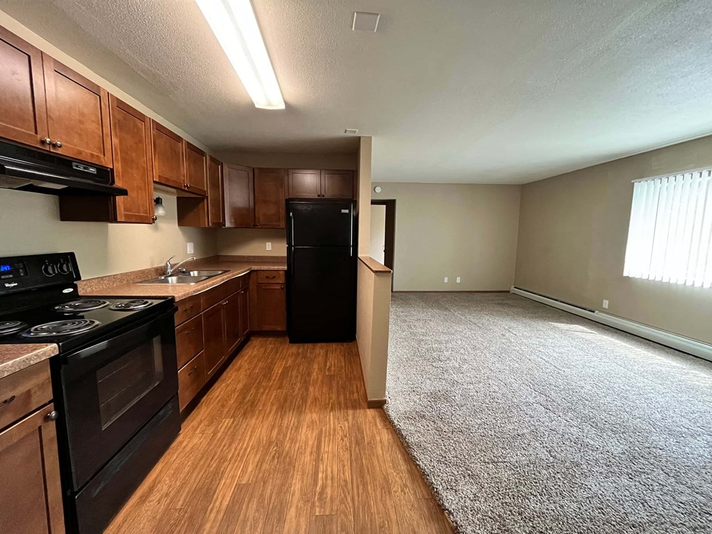 an empty kitchen and living room with wood floors and black appliances