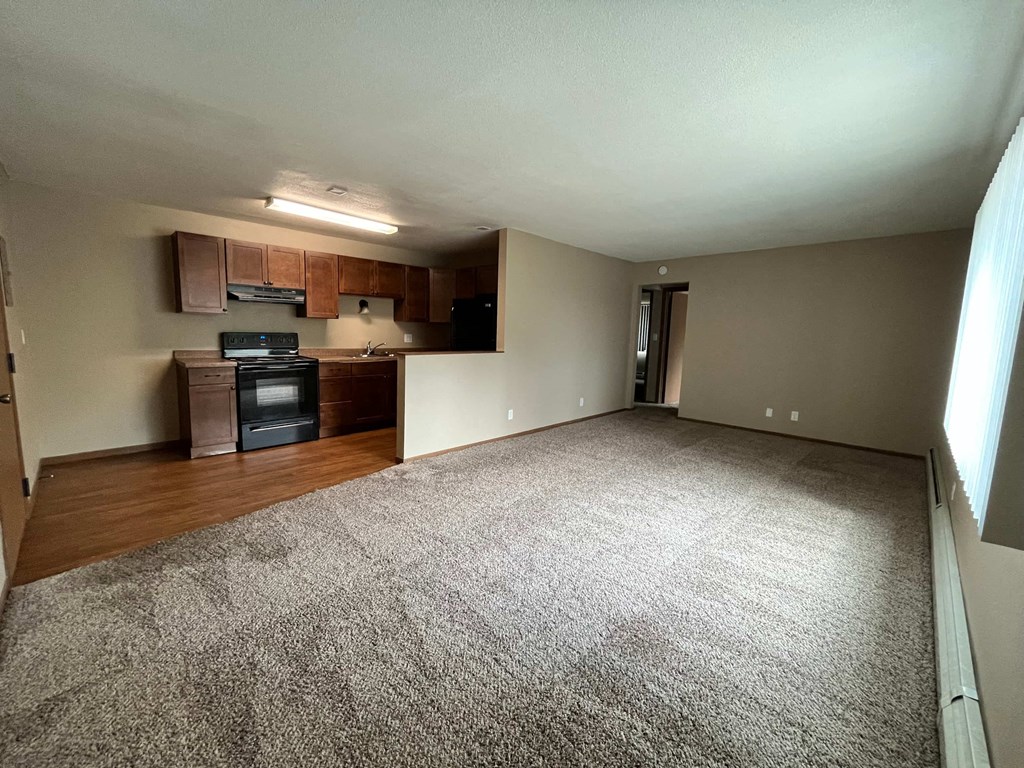an empty living room with wood flooring and a kitchen