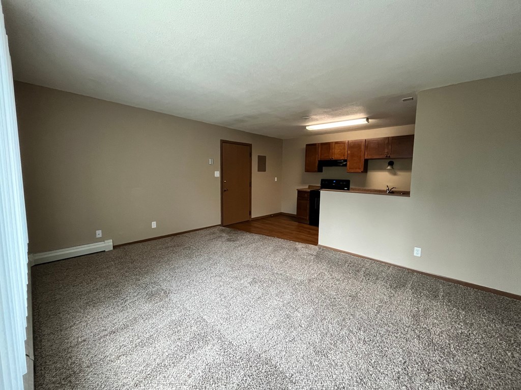 an empty living room with a kitchen in the corner