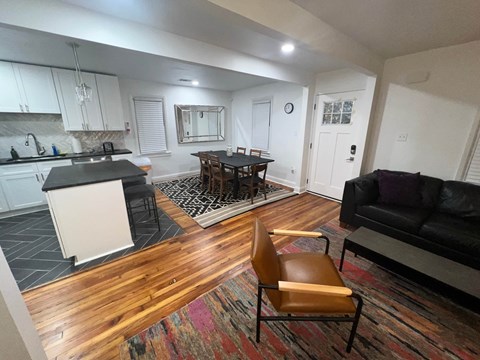 A black couch sits in a living room with a wooden floor and a rug.