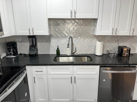 A kitchen with white cabinets and a black countertop.